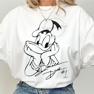 May include: White t-shirt with a black and white illustration of Donald Duck with his signature. The text "Donald Duck #1" is written below the illustration.