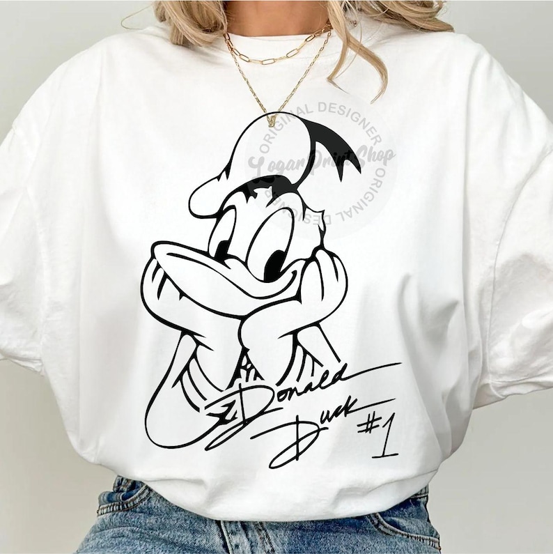 May include: White t-shirt with a black and white illustration of Donald Duck with his signature. The text "Donald Duck #1" is written below the illustration.