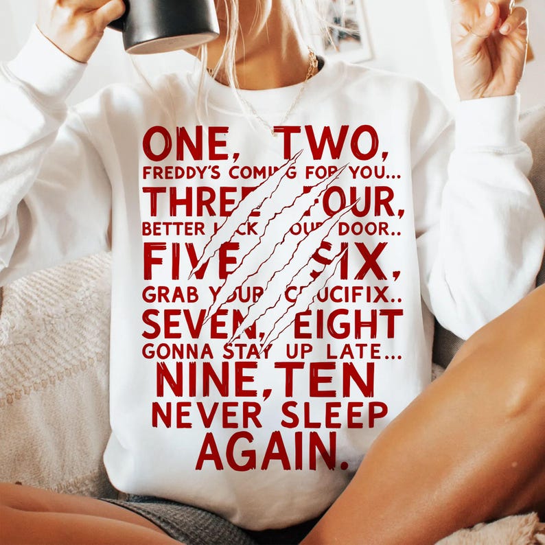 May include: White sweatshirt with the text "ONE, TWO, FREDDY'S COMING FOR YOU..." in red. The design includes claw marks. The sweatshirt is a casual garment.