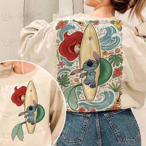 May include: Cream sweatshirt with a colourful graphic of Ariel, Stitch, and a surfboard. The design includes ocean waves, flowers, and a ukulele. The sweatshirt is a casual, comfortable style.