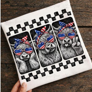 May include: White decorative towel featuring three Highland cows with heart-shaped sunglasses in the colors of the American flag. Each cow wears a patriotic bow. The towel has a black and white checkered border.