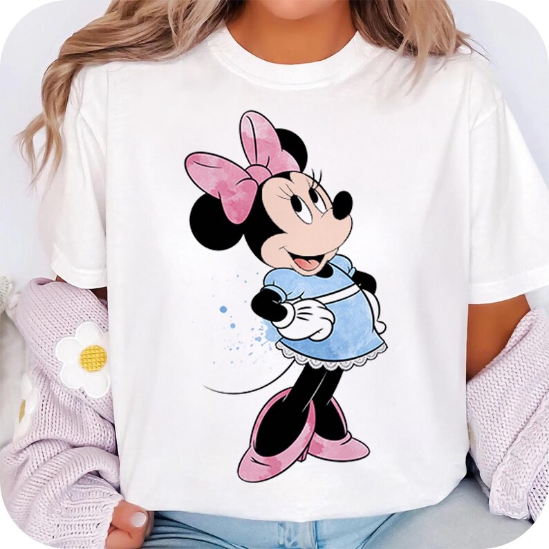 May include: White t-shirt with a cartoon image of Minnie Mouse wearing a blue dress and a pink bow.