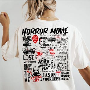 May include: Cream-colored t-shirt featuring a graphic design with the words "HORROR MOVIE" and various horror movie references. The design includes images of iconic horror characters and phrases like "Serial Killer Documentaries and Chill."