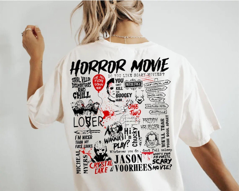 May include: Cream-colored t-shirt featuring a graphic design with the words "HORROR MOVIE" and various horror movie references. The design includes images of iconic horror characters and phrases like "Serial Killer Documentaries and Chill."