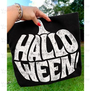 Op de afbeelding: Een zwart T-shirt met een grote, witte afbeelding in de vorm van een pompoen met een verweerde textuur, met de tekst "HALLOWEEN!" in dikke hoofdletters. Het ontwerp is gecentreerd op de voorkant van het kledingstuk en toont een vintage print.