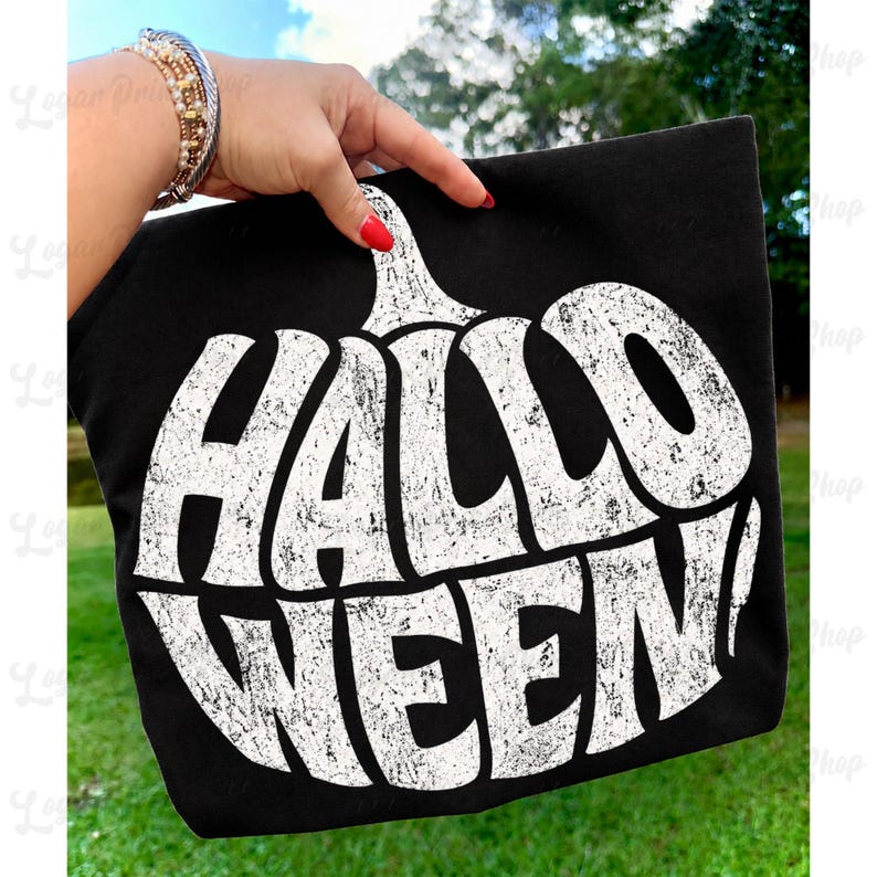 Op de afbeelding: Een zwart T-shirt met een grote, witte afbeelding in de vorm van een pompoen met een verweerde textuur, met de tekst "HALLOWEEN!" in dikke hoofdletters. Het ontwerp is gecentreerd op de voorkant van het kledingstuk en toont een vintage print.