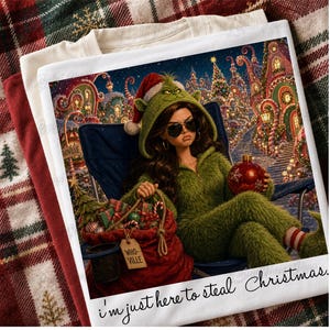 May include: A white t-shirt featuring a graphic of a person in a green fuzzy hooded outfit and sunglasses sitting in a chair, holding a red ornament next to a red sack labeled "WHO-VILLE". The text "i'm just here to steal Christmas" is printed below.
