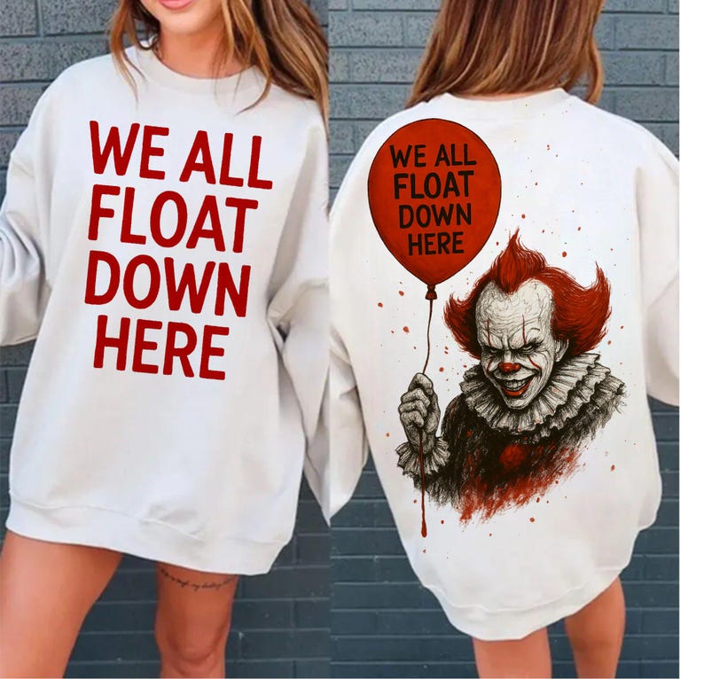 May include: White sweatshirt with the text "WE ALL FLOAT DOWN HERE" in red. The back features a graphic of a clown holding a red balloon with the same text. The clown has red hair and a sinister smile.