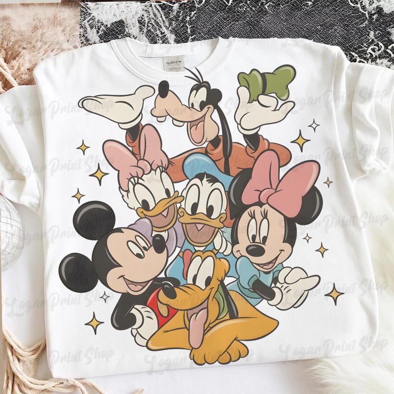 May include: White t-shirt featuring a colorful graphic of Disney characters Mickey Mouse, Minnie Mouse, Donald Duck, Daisy Duck, Goofy, and Pluto. The design includes yellow stars and is a fun, playful design.