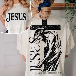 Puede incluir: Camiseta color crema con la palabra "JESUS" en letras negras grandes en la parte delantera. La parte trasera presenta un gráfico negro de Jesús en una cruz, con la palabra "JESUS" verticalmente y el texto "JESUS DIED FOR ME NOW I LIVE FOR HIM".
