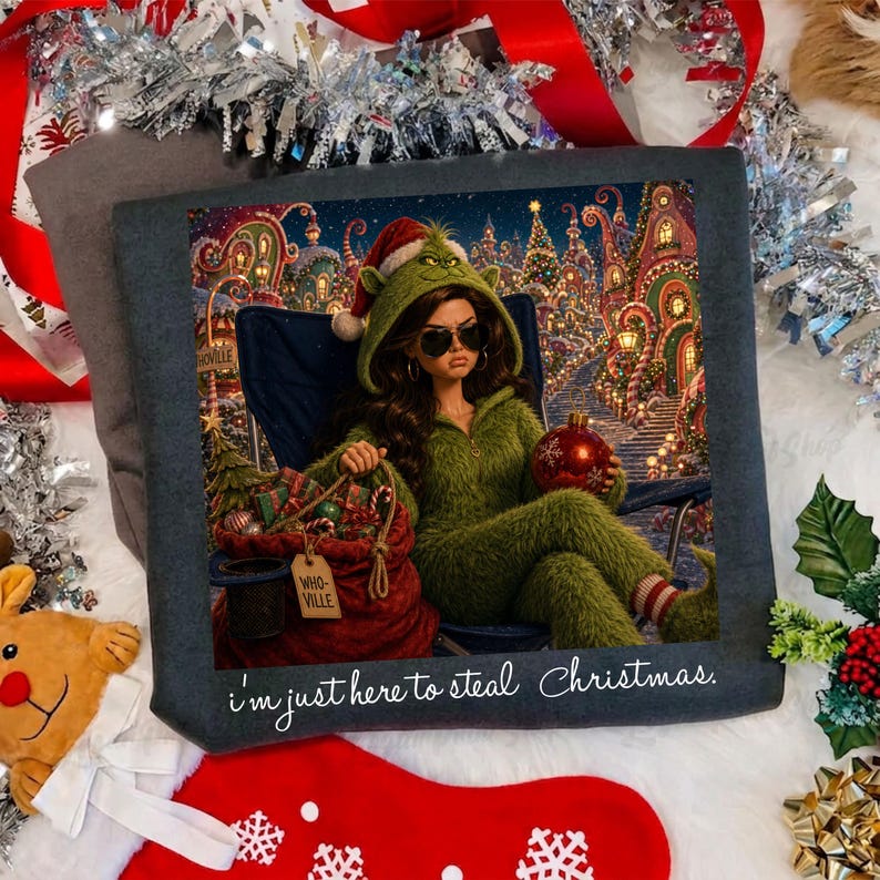 May include: A dark gray sweatshirt featuring a graphic print of a person in a green fuzzy hooded outfit, sunglasses, and a Santa hat, sitting in a chair with a red sack labeled "WHO-VILLE" and the text "I'm just here to steal Christmas."