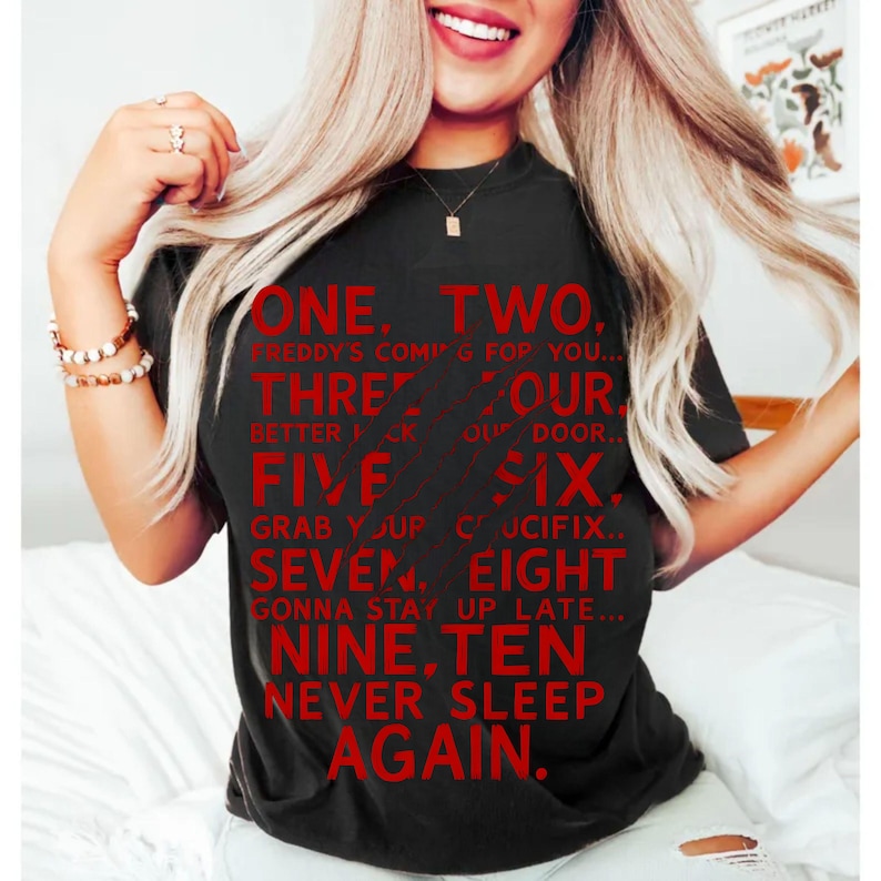 May include: Black t-shirt with red text. The text reads "ONE, TWO, FREDDY'S COMING FOR YOU... THREE, FOUR, BETTER LOCK YOUR DOOR... FIVE, SIX, GRAB YOUR CRUCIFIX... SEVEN, EIGHT, GONNA STAY UP LATE... NINE, TEN, NEVER SLEEP AGAIN."