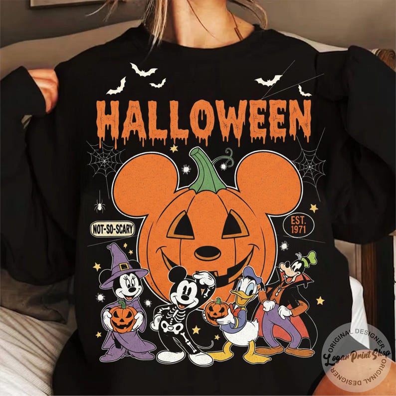 May include: Black Halloween sweatshirt featuring a large orange pumpkin with Mickey Mouse ears and a smiling face. The word "HALLOWEEN" is above the pumpkin, with bats and cartoon characters below. Text includes "NOT-SO-SCARY" and "EST. 1971."