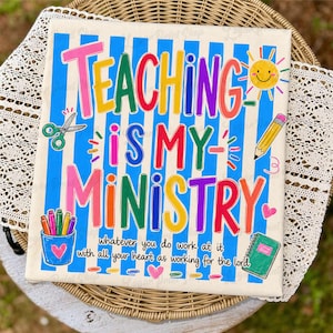 May include: A colorful canvas print with the text "TEACHING IS MY MINISTRY" in various bright colors. The background has blue vertical stripes. The image includes illustrations of a smiling sun, scissors, a pencil, and a notebook.