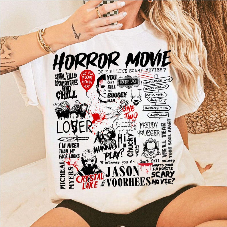 May include: White t-shirt with a graphic design featuring horror movie characters and phrases. The design includes text like "HORROR MOVIE", "SERIAL KILLER", and "FREDDY KRUEGER". The shirt has a crew neck and short sleeves.