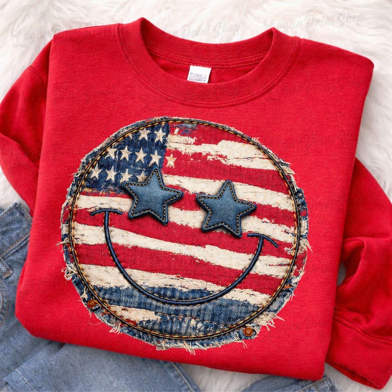 May include: Red sweatshirt featuring a distressed American flag smiley face design. The smiley face has denim star eyes and a stitched denim border. The design is centered on the front of the sweatshirt.