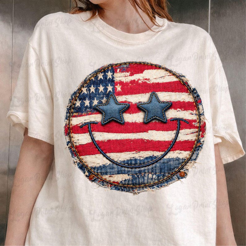 May include: Cream-colored t-shirt featuring a distressed American flag smiley face design. The smiley face has blue star eyes and a stitched denim border. The shirt is a casual, patriotic style.