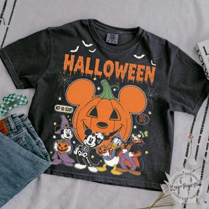 May include: Black t-shirt with a Halloween graphic featuring Mickey Mouse, Donald Duck, Goofy, and a pumpkin. The orange text reads "HALLOWEEN" and "NOT-SO-SCARY". The design includes bats and spiderwebs, with "EST. 1971".