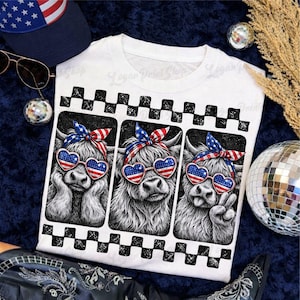 May include: White t-shirt featuring three Highland cows wearing heart-shaped sunglasses with an American flag design and patriotic headbands. The shirt has a black and white checkered border design. A navy blue hat with stars and sunglasses are visible.