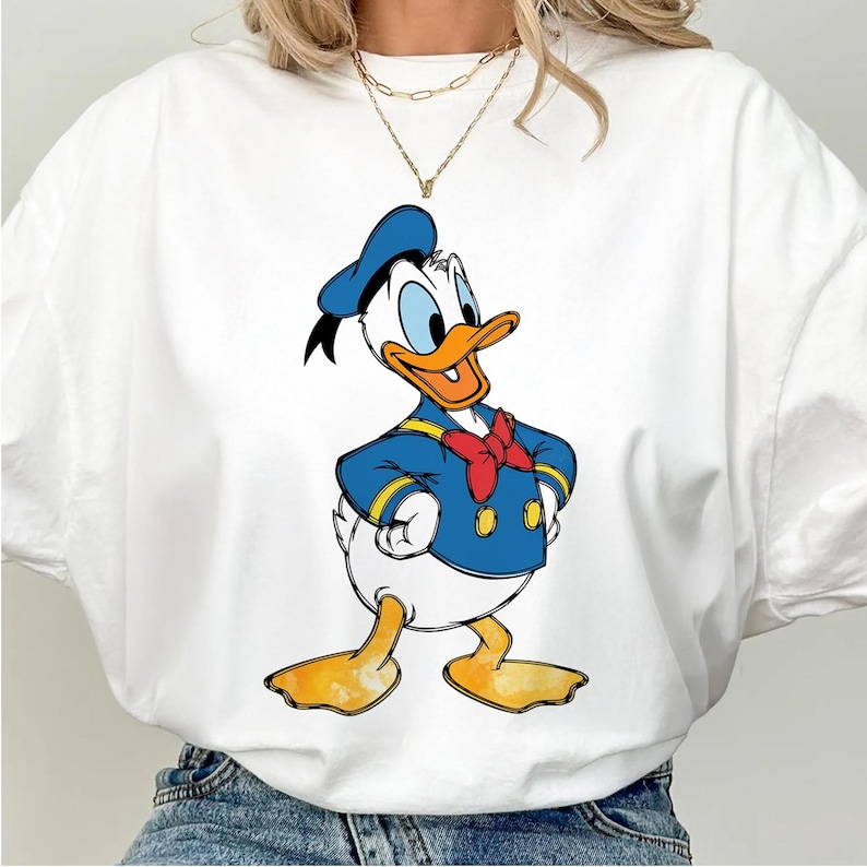 May include: White t-shirt with a cartoon image of Donald Duck wearing a blue sailor outfit and a red bow tie.