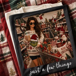 May include: A black t-shirt featuring a graphic print of a person wearing a Grinch-themed sweater and sunglasses, standing in a store aisle filled with Christmas decorations and a shopping cart. The text "just a few things" is printed at the bottom.