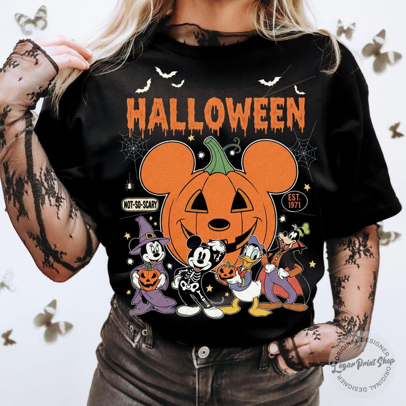 May include: Black Halloween t-shirt featuring a large orange pumpkin with Mickey Mouse ears and the word "HALLOWEEN" in orange. Below the pumpkin are cartoon characters in Halloween costumes. The shirt has the text "NOT-SO-SCARY" and "EST. 1971".