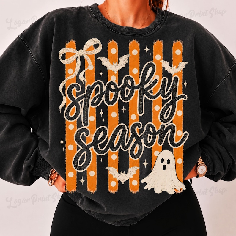 Op de afbeelding: Een zwart acid-wash sweatshirt met ronde hals en een grafische print met verticale oranje en witte stippenstrepen. Het ontwerp bevat een grote witte strik, drie vliegende vleermuizen, een wit spook en de zwarte cursieve tekst Spooky Season.