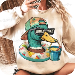 May include: A beige sweatshirt featuring a cartoon duck wearing sunglasses with "SUMMER VIBES" text. The duck is wearing a hat and a life ring. It holds a blue bucket with sand and a red shovel. The design has a summer theme.