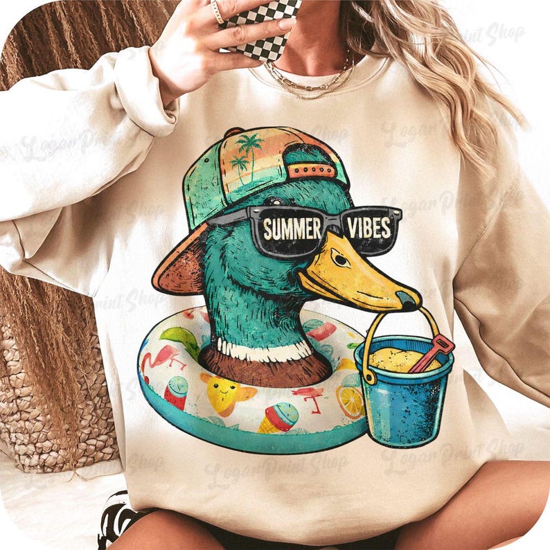 May include: A beige sweatshirt featuring a cartoon duck wearing sunglasses with "SUMMER VIBES" text. The duck is wearing a hat and a life ring. It holds a blue bucket with sand and a red shovel. The design has a summer theme.