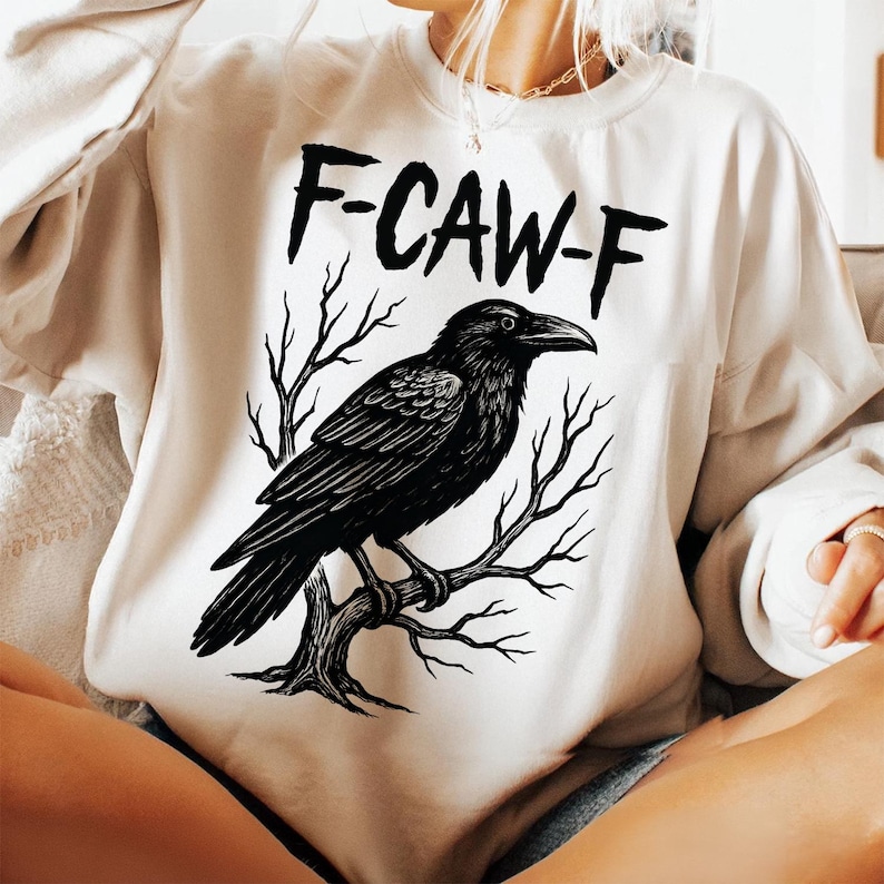 May include: Cream-colored sweatshirt with a black graphic of a raven perched on a tree branch. The text "F-CAW-F" is above the raven. The design is centered on the front of the sweatshirt.