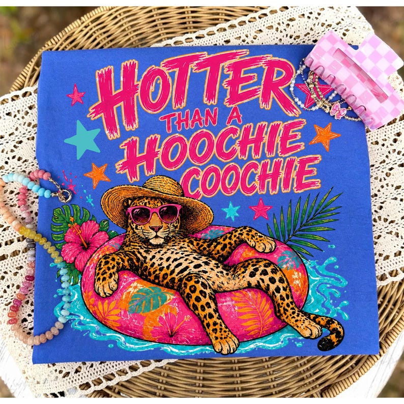 Puede incluir: Camiseta azul con el texto rosa "Hotter Than A Hoochie Coochie". El dise&ntilde;o presenta un leopardo con gafas de sol y sombrero de paja, descansando en un flotador inflable rosa. Estrellas y flores tropicales.