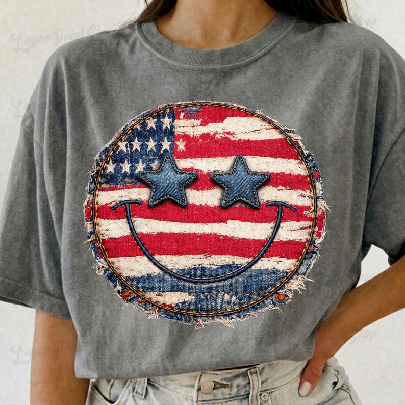 May include: Gray t-shirt featuring a distressed smiley face design. The smiley face incorporates the American flag with blue star-shaped eyes and a denim-like border. The design is centered on the shirt.