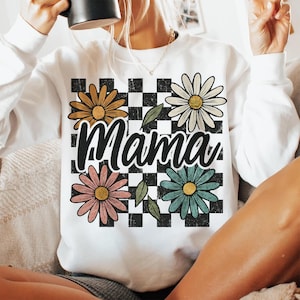 May include: White sweatshirt with a black and white checkered pattern, four colorful daisies, and the word "Mama" in black.