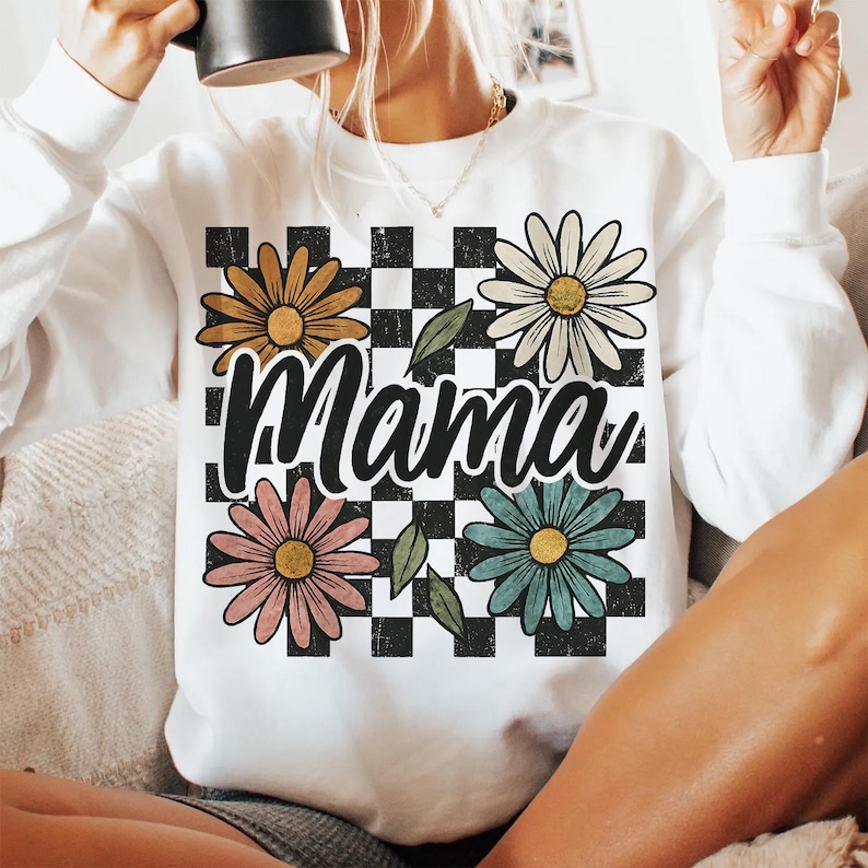 May include: White sweatshirt with a black and white checkered pattern, four colorful daisies, and the word "Mama" in black.