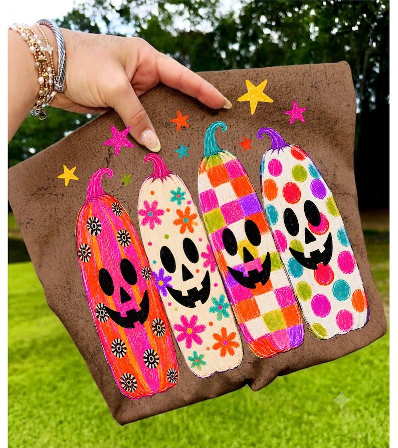 May include: A brown fabric pouch featuring a colorful graphic of four tall, slender pumpkins with jack-o'-lantern faces. The pumpkins are decorated with bright floral, checkered, and polka dot patterns in pink, orange, green, and blue, with small stars.