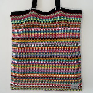 May include: A colorful striped crochet tote bag with black straps and a black fabric lining. The bag has a small black tag with the word "NORTE" on it.