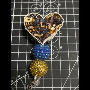 May include: A heart-shaped badge reel featuring a Harry Potter design with Hogwarts castle, a sorting hat, and the text "Always, It's Irvin's". The reel has blue and gold rhinestone accents.