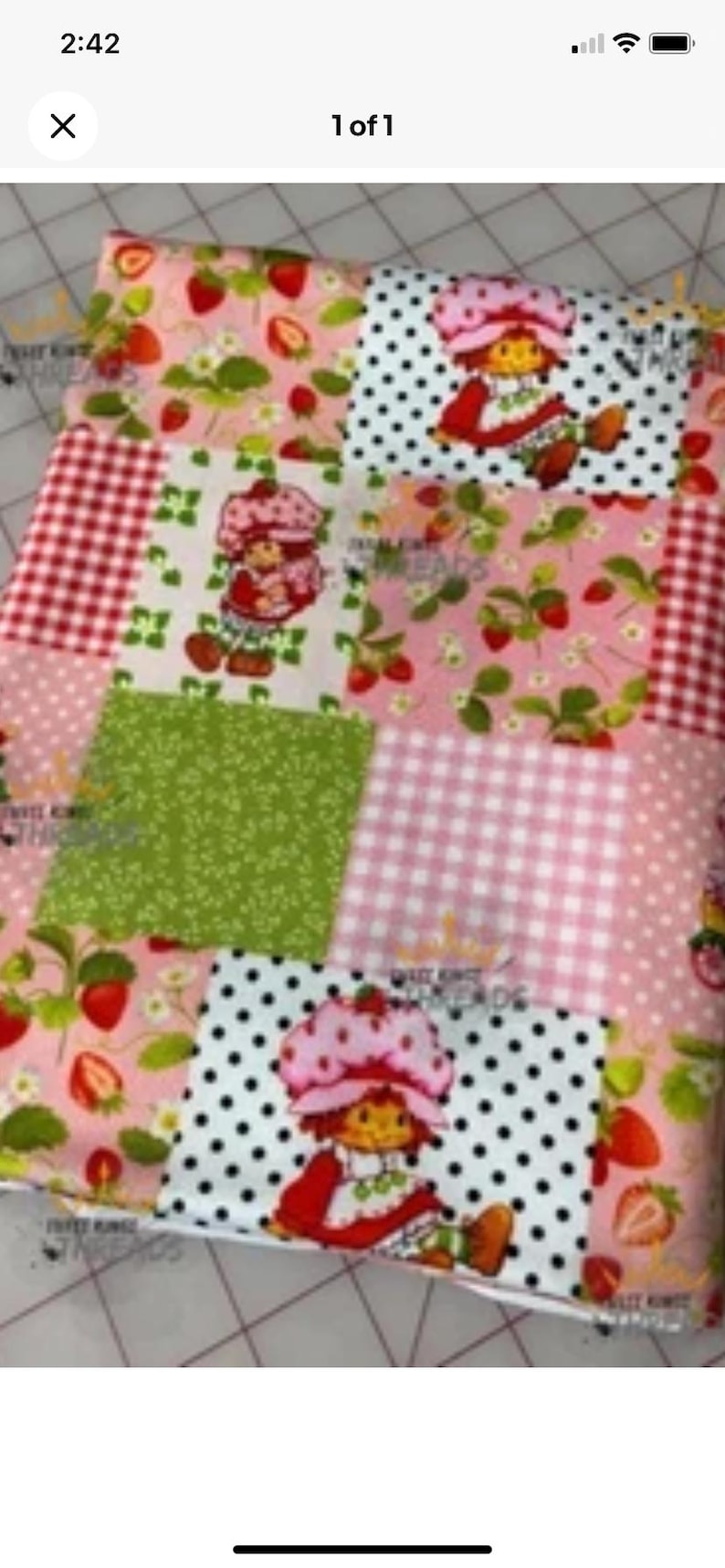 May include: A patchwork fabric featuring various patterns, including red gingham, white polka dots, and strawberry motifs. The design incorporates images of a cartoon character with a strawberry hat. The color palette includes pink, red, green, and white.