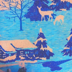 May include: A fabric featuring a winter landscape print in shades of blue and light peach. The pattern displays snow-covered pine trees, a cabin, and two deer standing in a field. The design includes a subtle metallic glitter effect throughout.