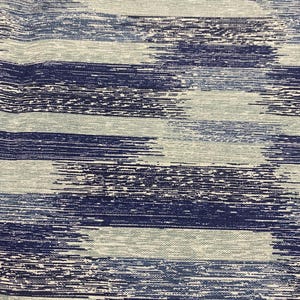 May include: Close-up of a fabric with a horizontal brushstroke pattern. The design features varying shades of blue and white, creating a textured, artistic effect. The fabric appears to be a woven material, suitable for apparel or home decor.