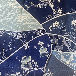 May include: Close-up of a fabric with a patchwork design in shades of blue and white. The fabric features floral and geometric patterns, including stylized flowers and wave-like motifs. The text "Indigo Patchwork by Connect" is visible at the bottom.