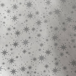 Puede incluir: Primer plano de una tela blanca con un patrón repetido de estrellas grises y pequeños puntos. Las estrellas varían en tamaño y tienen múltiples puntas, creando un diseño celestial. La tela tiene una textura sutil.
