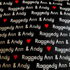 May include: Black fabric with a repeating pattern of the text "Raggedy Ann & Andy" in white script, interspersed with small red hearts. The design is a classic and nostalgic theme.