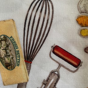 May include: A white fabric featuring a repeating kitchen pattern with a brown wire whisk, a block of butter labeled FRESH BUTTER, a red-handled pastry cutter, and various small bowls containing colorful ingredients like yellow spices and white flour.