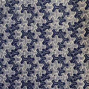 May include: Close-up of a fabric with a repeating pattern of dark blue geometric shapes and text on a cream background. The shapes are arranged in a grid-like fashion, creating a textured appearance. The fabric has a vintage or retro aesthetic.