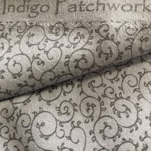 Puede incluir: Primer plano de una tela con fondo gris y un patrón repetitivo de diseños florales grises oscuros en espiral. El texto "Indigo Patchwork" es visible en la parte superior. La tela tiene un aspecto texturizado.