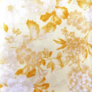 May include: A woven fabric featuring a repeating floral pattern in shades of golden yellow and cream. The design consists of various blossoms and leaves scattered across the surface, creating a dense botanical print on the textile.