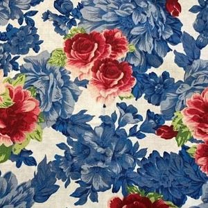 May include: A white fabric with a floral pattern featuring large blue and red roses. The fabric has a vintage feel and would be perfect for crafting projects.
