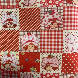 Puede incluir: Una tela de patchwork con un patrón repetido de personajes de Strawberry Shortcake, gatos rosas y varios diseños rojos y blancos. La tela está dividida en cuadrados con patrones de cuadros, rayas y flores.