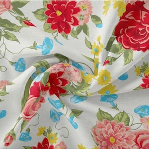 May include: White fabric with a floral pattern featuring red, pink, yellow, and blue flowers. The fabric is wrinkled and has a soft, flowing texture.